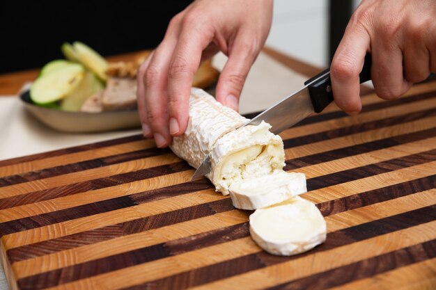 Mani che tengono e che tagliano formaggio a pasta molle sul bordo di legno