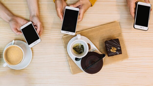 Mani che tengono gli smartphone con tè e caffè