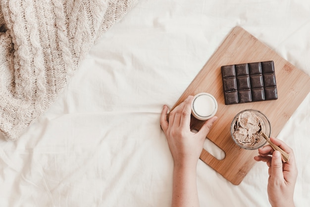 Mani che tengono il latte e mescolando i cornflakes nel letto