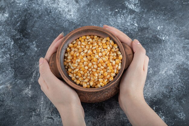 Mani che tengono un'antica ciotola piena di semi di popcorn crudi.