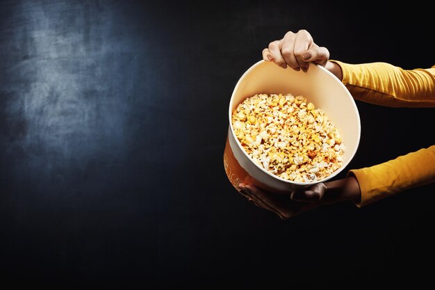 Mani che tengono un grande secchio di popcorn dolci e salati caldi