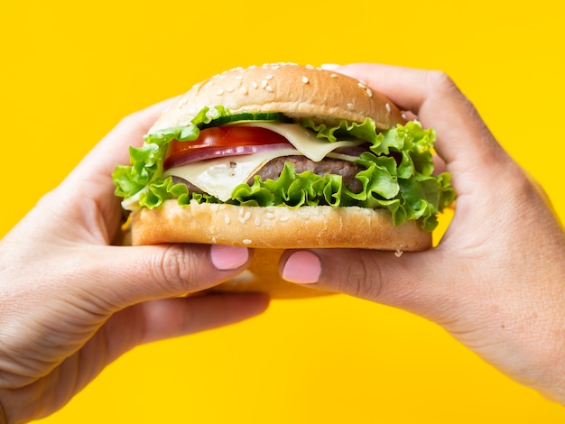 Mani che tengono un hamburger su fondo giallo