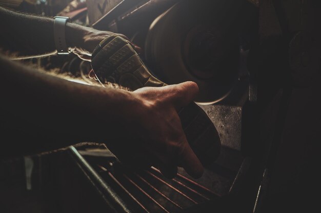 Mani del maestro di scarpe, che sta lavorando sulla suola della scarpa, utilizzando una macchina utensile speciale.