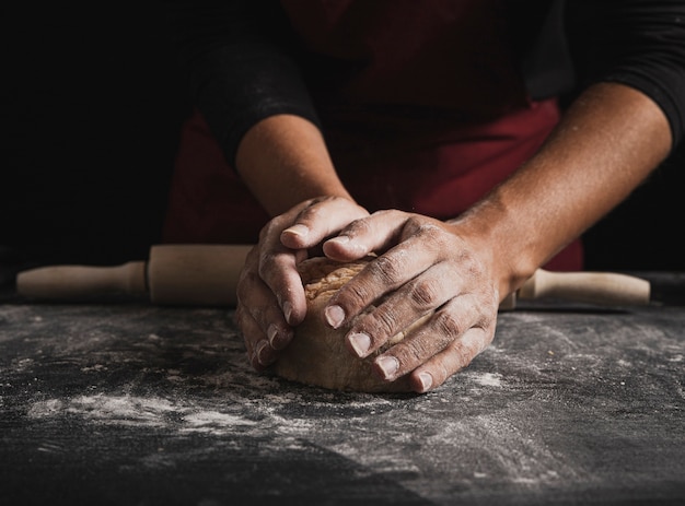 Mani del panettiere del primo piano che impastano pasta