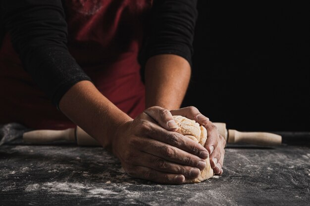 Mani del panettiere del primo piano che impastano pasta