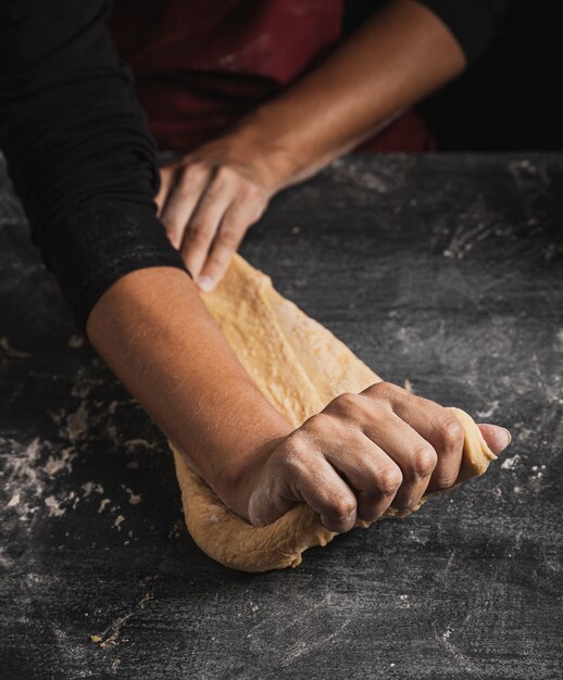 Mani del panettiere del primo piano che impastano sulla composizione superiore nella pasta