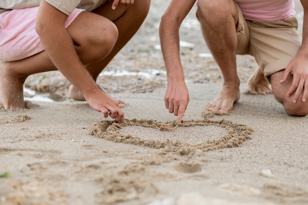 Mani del primo piano che disegnano cuore sulla sabbia