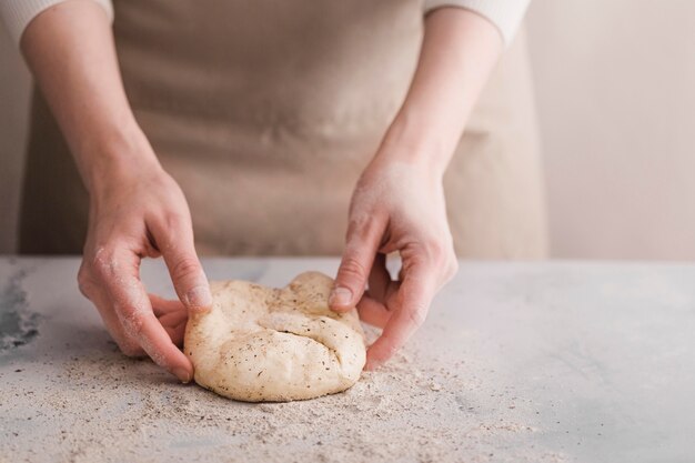 Mani del primo piano che impastano la pasta di pane