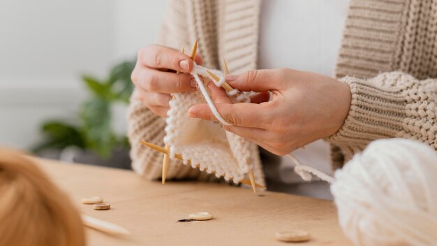 Mani del primo piano che lavorano a maglia con filato bianco