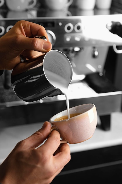 Mani del primo piano che preparano caffè con latte