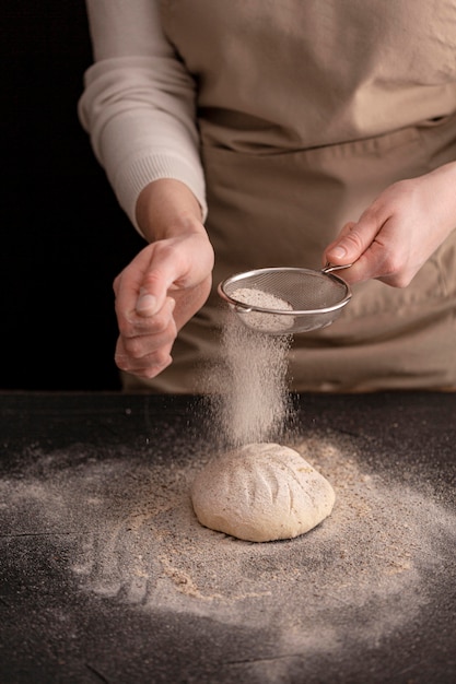 Mani del primo piano che producono pane con farina