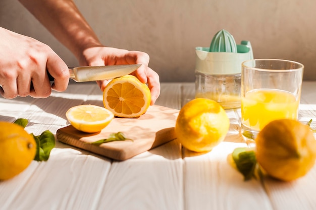 Mani del primo piano che tagliano limone con il coltello