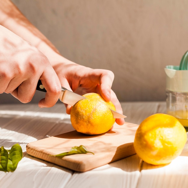 Mani del primo piano che tagliano limone