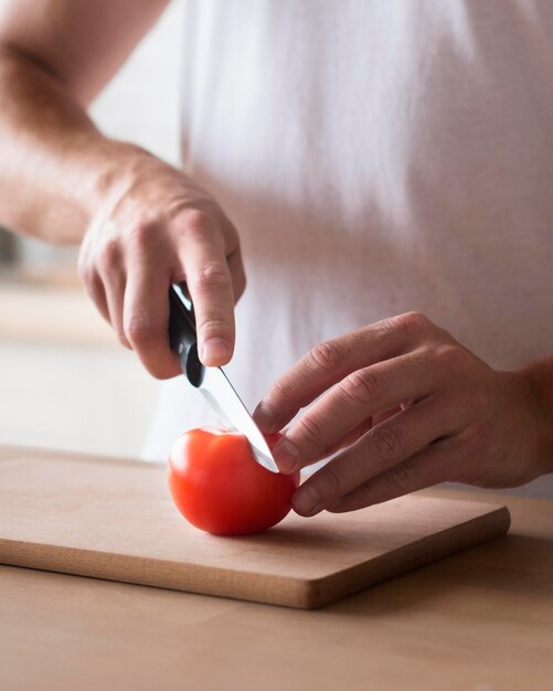 Mani del primo piano che tagliano pomodoro
