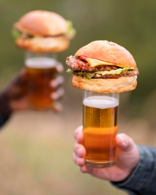 Mani del primo piano che tengono birra e hamburger