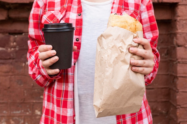 Mani del primo piano che tengono caffè e alimento