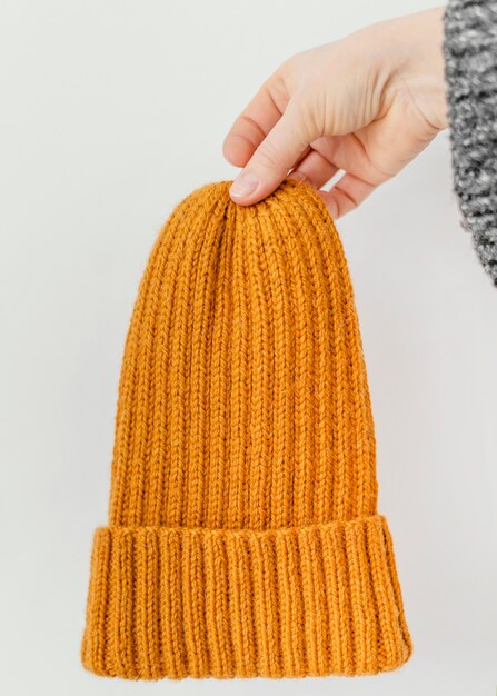 Mani del primo piano che tengono il cappello lavorato a maglia arancione