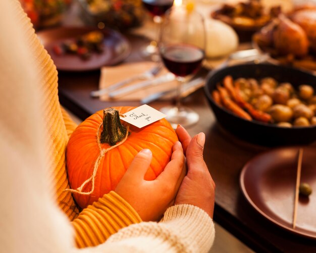 Mani del primo piano che tengono la zucca al tavolo