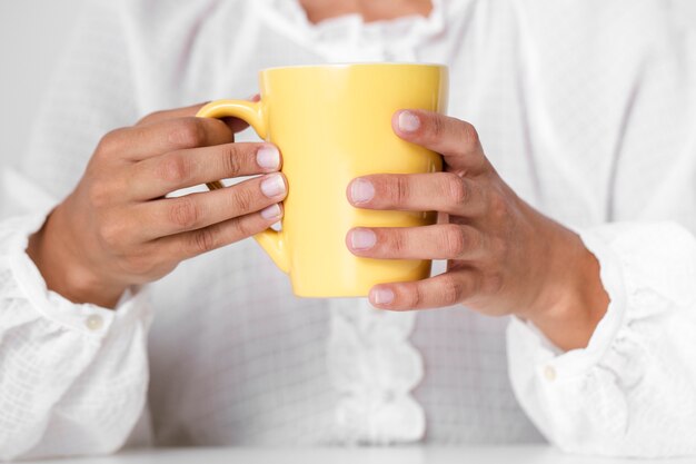 Mani del primo piano che tengono tazza gialla