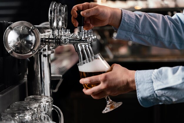 Mani del primo piano che versano birra in vetro