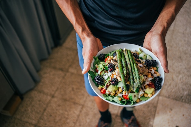 Mani dell'uomo che tengono grande piatto profondo pieno di sana insalata vegetariana paleo