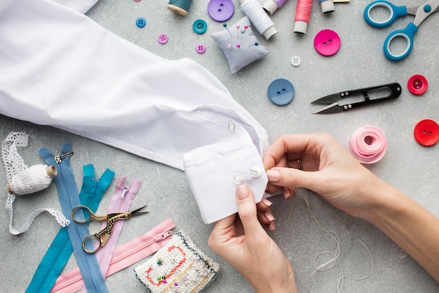 Mani della donna che cuce una vista superiore della camicia bianca