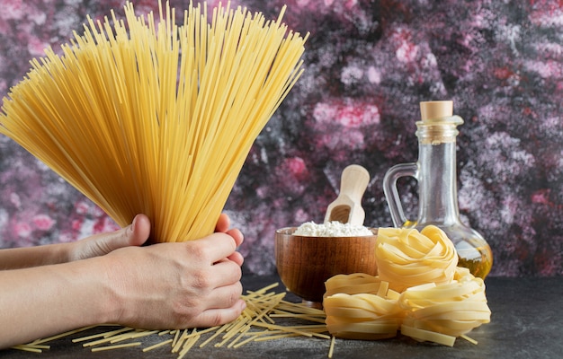 Mani della donna che tengono gli spaghetti sul colorato con olio e farina.