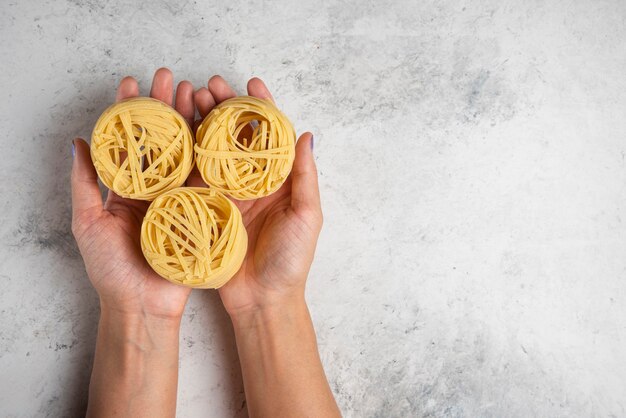 Mani della donna che tengono i nidi di pasta tagliatelle crude su priorità bassa bianca.