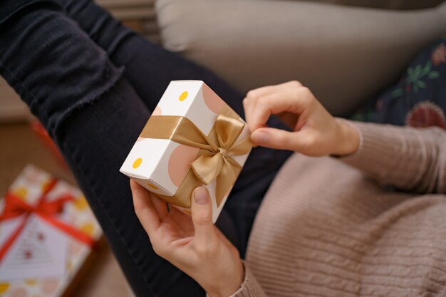 Mani della donna che tengono scatola bianca avvolta con fiocco dorato, concentrarsi sulla scatola