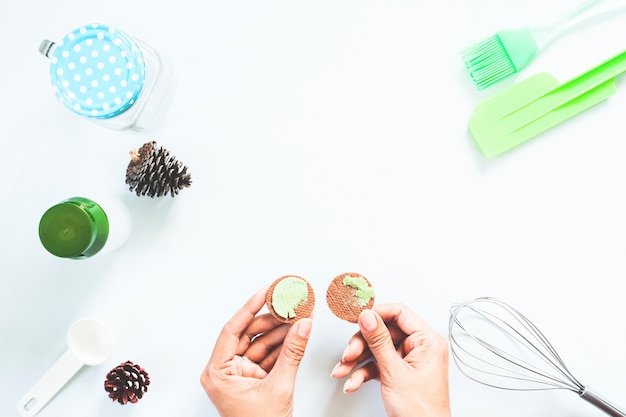 Mani della donna con la crema di tè verde di macha e biscotti utensili da forno su tavola bianca, Flat lay