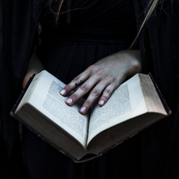 Mani della donna in vestiti neri che tengono libro aperto