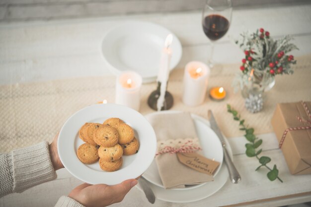 Mani della donna irriconoscibile che mettono il piatto di biscotti sulla tavola adorabile di Natale