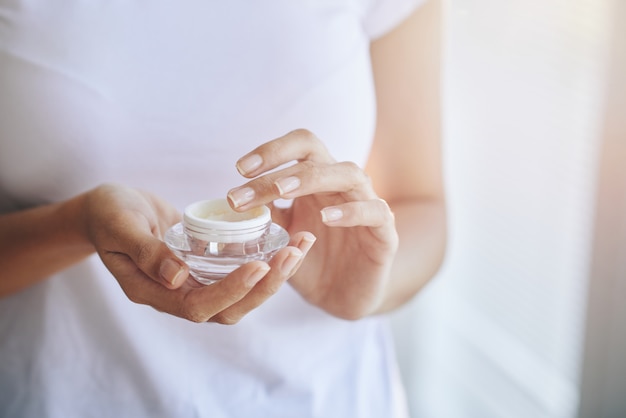 Mani della donna irriconoscibile che raccolgono la crema per il viso dal vaso