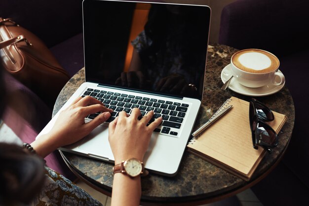 Mani della donna irriconoscibile che scrivono sul computer portatile in caffè
