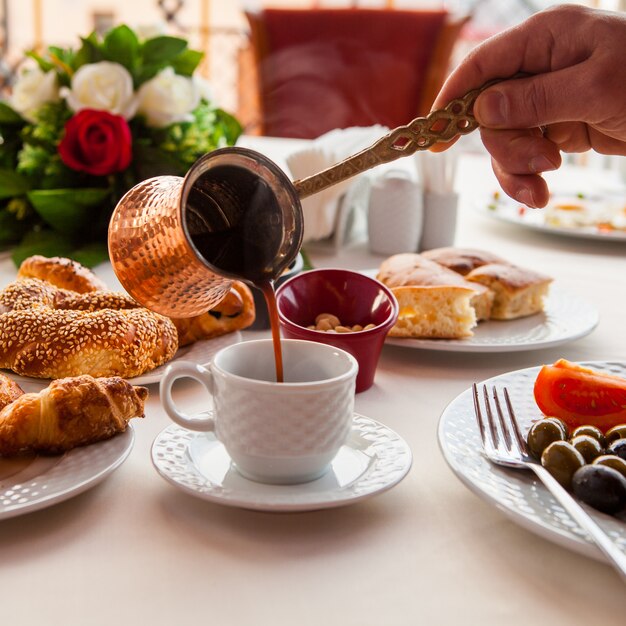 Mani della prima colazione del primo piano con il caffè di versamento di jezve nella tazza bianca, panini