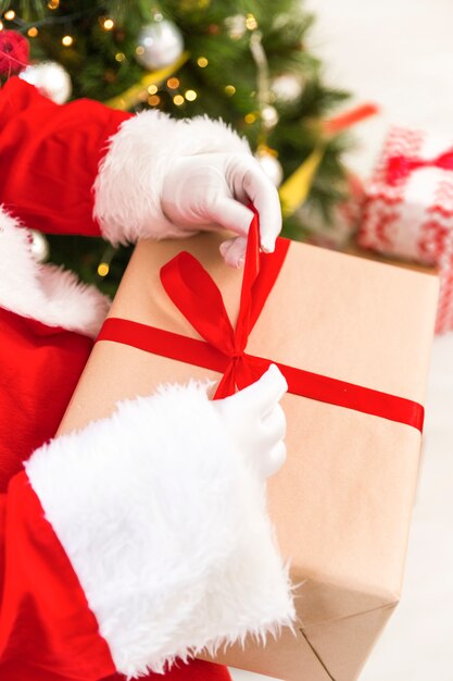 Mani di Babbo Natale che avvolgono regalo con nastro