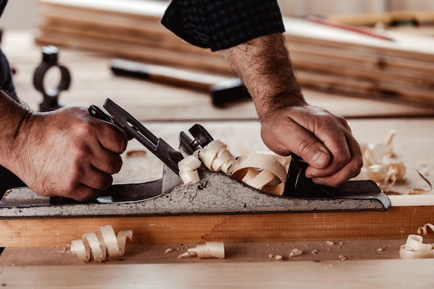 Mani di carpentieri che piallano una tavola di legno con una pialla a mano