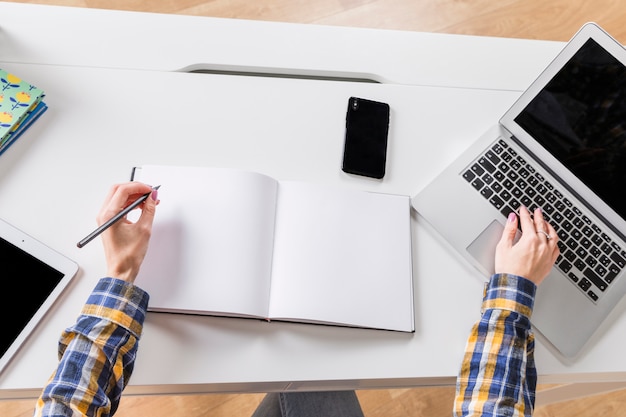 Mani di donna che scrive in taccuino e toccando la tastiera del computer portatile