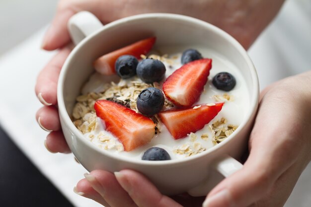 Mani di donna che tengono una ciotola con gustosi muesli con frutta, avena e yogurt. Avvicinamento. Concetto di alimento sano.