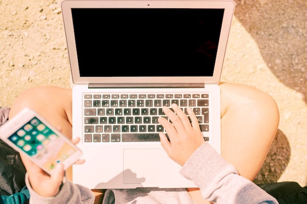 mani di libero professionista che digitano sul computer portatile durante l&#39;utilizzo di smartphone