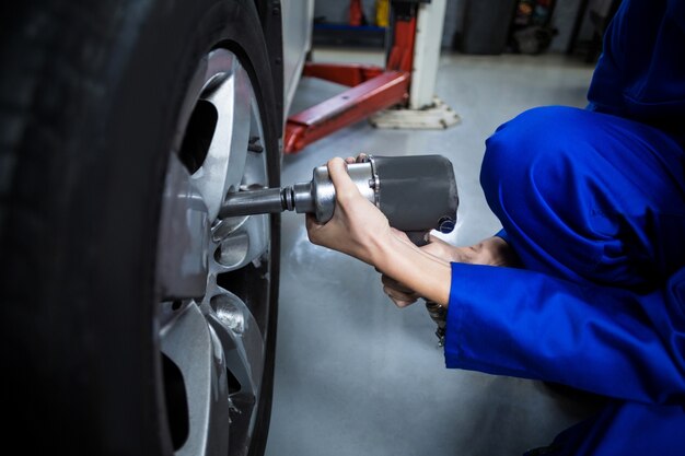 Mani di meccanico femminile di fissaggio di una ruota auto con la chiave pneumatica