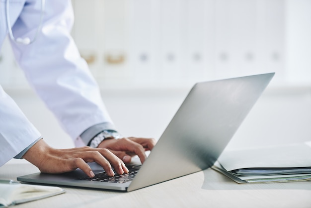 Mani di medico femminile irriconoscibile che utilizza computer portatile nell'ufficio