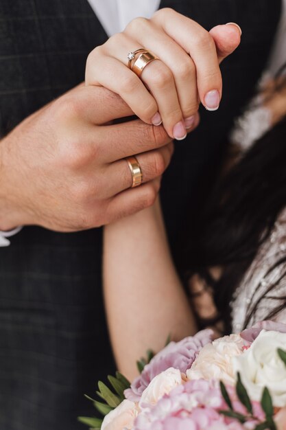 Mani di una moglie e un marito con anelli di fidanzamento e matrimonio e parte del bouquet floreale