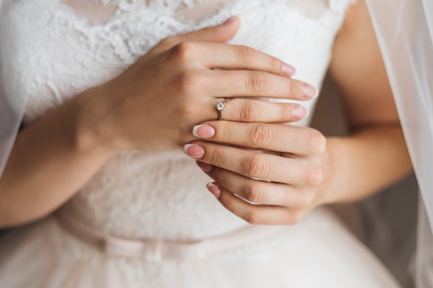 Mani di una sposa con tenera manicure francese e prezioso anello di fidanzamento con diamante lucido, abito da sposa