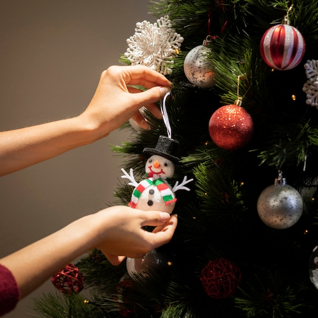 Mani di vista frontale che mettono i globi sull'albero di Natale