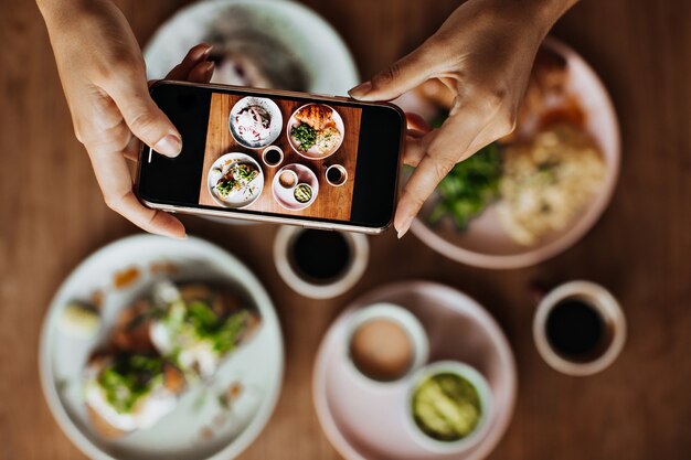 Mani femminili abbronzate che tengono smartphone e scattare foto del piatto con il pasto