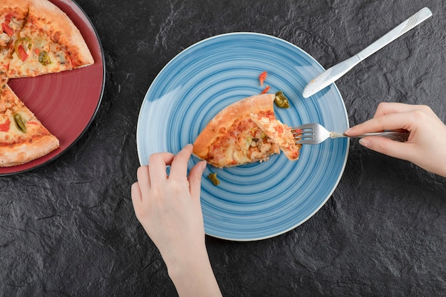 Mani femminili che prendono fetta di pizza dalla piastra su sfondo nero.