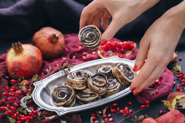 Mani femminili che prendono il rotolo di cucciolo vegano crudo da una placca di metallo con semi di rosa canina e melograno