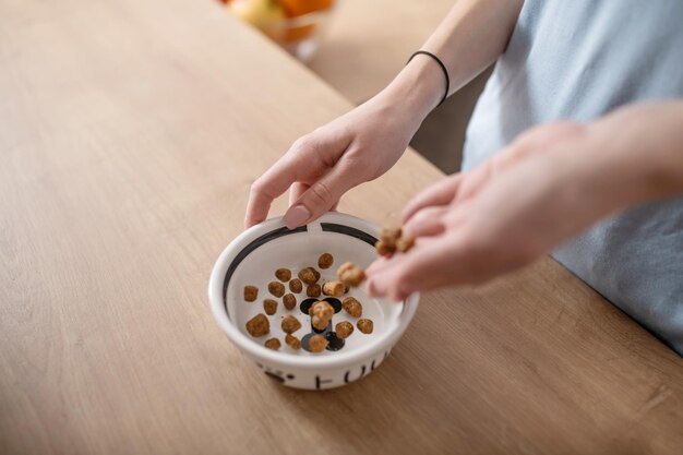 Mani femminili che riempiono la ciotola con cibo per cani secco