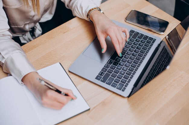 Mani femminili che scrivono sul blocco note e lavorano al computer